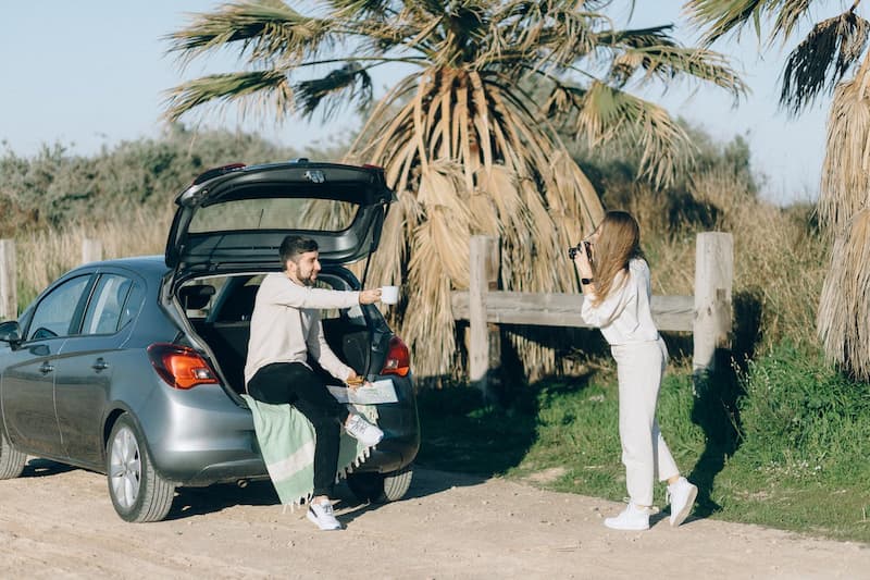 Пара туристов на машине остановились на дороге с пальмами, чтобы сделать фото